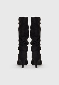 Bottes noires en suède, montantes jusqu'au genou, avec un design décontracté et un talon aigu haut, présentant une texture lisse et un minimalisme dans les détails.