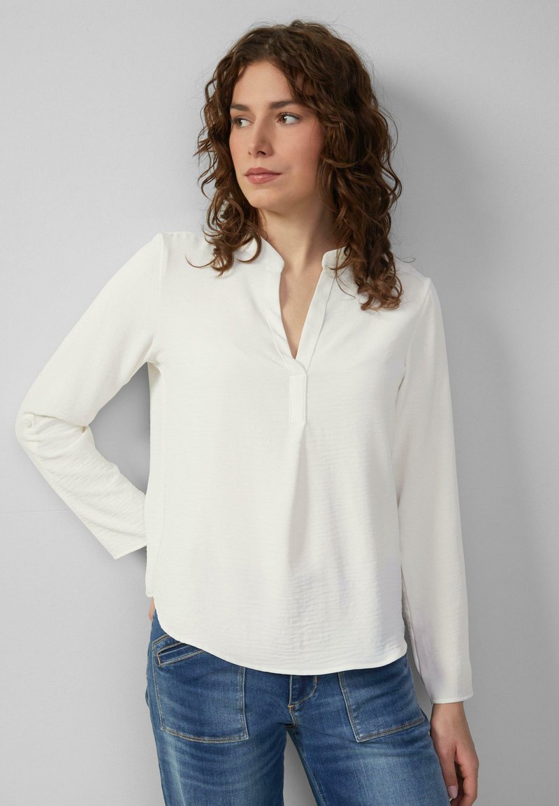 Witte long-sleeve shirt met een V-hals, zachte textuur en een licht gebogen zoom, gecombineerd met blauwe denim jeans.