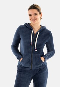 Sudadera con cremallera de pana en color navy, con capucha ajustable, bolsillos frontales y textura acanalada. Combinada con pantalones a juego.