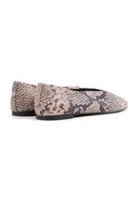 Zapatos planos en un patrón de serpiente beige y negro, elaborados con materiales texturizados, con un diseño delgado y una suela negra baja.