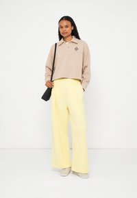 Suéter bege recortado com gola com colarinho e bordado às riscas, combinado com calças largas amarelas de cintura alta e sapatos claros.