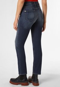 Mörkblå denimjeans med smal passform, utrustade med bakfickor och detaljer i sömmar. Matchade med svarta ankelstövlar mot en ljus bakgrund.