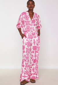 Combinaison à motifs floraux en blanc et rose, avec un col en V, des manches trois-quarts, une taille élastiquée avec cordon et des pantalons larges.