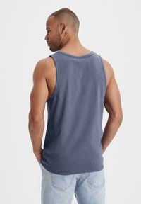Blue sleeveless tank top with a rounded neckline, made from a lightweight fabric; worn with light blue jeans. Smooth texture, casual fit.
