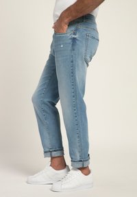 Jeans in denim azzurro chiaro con una vestibilità comoda, dettagli strappati e orli arrotolati, abbinati a sneaker bianche.