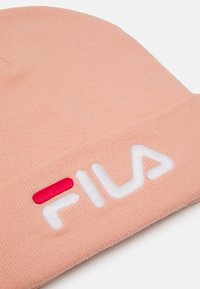Világos rózsaszín kötött sapka, feltűnő fehér "FILA" logóval és piros kiegészítéssel, puha textúrával és szoros illeszkedéssel.