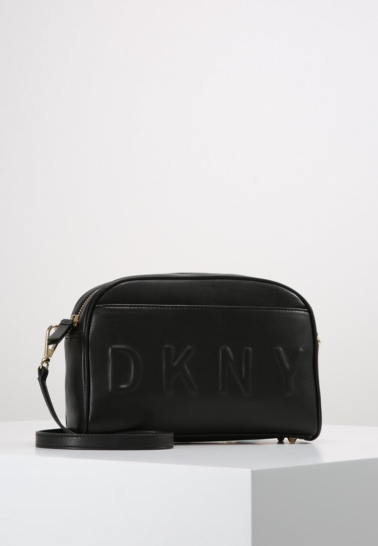 Borsa a tracolla rettangolare nera con logo DKNY impresso, zipper dorato e tracolla regolabile, posizionata su una superficie bianca.