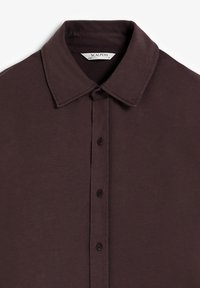 Camisa marrón de botones hecha de una tela suave, con un collar clásico, botones en el frente y un diseño sencillo sin patrones ni acentos.