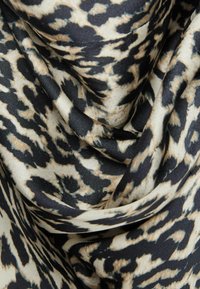 Šátek s leopardím potiskem, kombinující béžovou a černou barvu, s hladkou texturou a jemným splývavým materiálem.