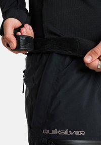 Schwarze Schnee-Hosen mit einem strukturierten Bund, der einen Velcro-Riemen aufweist, Reißverschlüsse an den Seitentaschen und gesticktem Quiksilver-Logo.