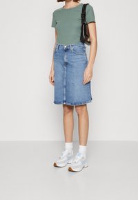 Top verde de manga corta con textura acanalada combinado con una falda midi de denim. Zapatillas blancas con toques de azul claro y calcetines completan el conjunto.