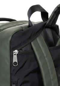 Mochila con exterior acolchado verde, base negra y cremallera plateada. Presenta una textura mate y un asa corta en la parte superior.