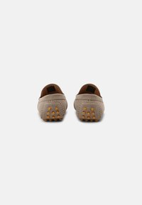 Beiga loafers i mjukt mockamaterial, bakvy som visar gummisula med upphöjda prickar för grepp och detaljerad sömnad runt kanterna.