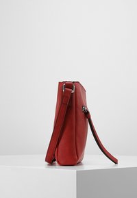 Czerwona skórzana torebka o smukłej sylwetce, z regulowanym paskiem i srebrnymi okuciami. Gładka tekstura, minimalistyczny design bez widocznych wzorów.