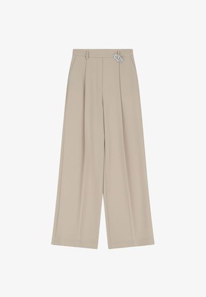 Pantaloni beige a gamba larga realizzati in tessuto morbido, con vita, pieghe frontali e un distintivo accentuato da una spilla di cristallo decorativa sul lato.