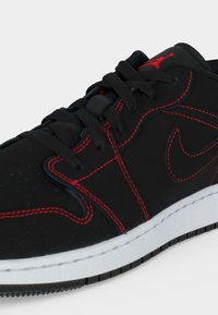 Μαύρο αθλητικό παπούτσι Nike με κόκκινες ραφές, μαύρα κορδόνια, κόκκινο λογότυπο Jumpman στη γλώσσα και λευκή σόλα με μαύρο ανάγλυφο μοτίβο.
