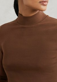Top aderente marrone con scollo alto, realizzato in tessuto a costine, dotato di maniche lunghe e design senza cuciture.
