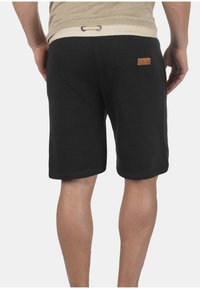 Zwarte katoenen shorts met een gestructureerd oppervlak, voorzien van een elastische tailleband en een enkele achterzak met een tan leren accent.