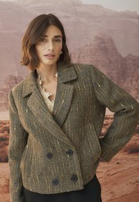 Braun-schwarz kariertes Blazer mit Hahnentrittmuster, doppelreihigem Design, Reverskragen und schwarzen Knöpfen mit strukturierter Oberfläche.