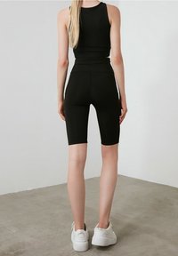 Crop top atletico nero e pantaloni leggings a vita alta, realizzati in un tessuto morbido e elasticizzato. Accentuati da un design pulito e minimalista, con sneakers bianche.