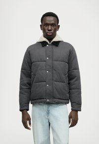 Jachetă gri căptușită cu guler căptușit cu sherpa, nasturi tip snap și buzunare laterale, asortată cu blugi de culoare albastru deschis.