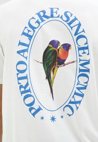 Camiseta blanca con un gráfico de dos aves coloridas en una rama, rodeadas de "PORTO ALEGRE SINCE MCMXC." Texto azul en negrita y acentos de estrellas.