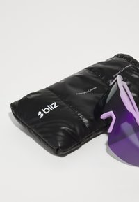Étui rembourré noir avec texte blanc, contenant des lunettes de soleil teintées de violet avec des branches angulaires et une finition lisse des verres.