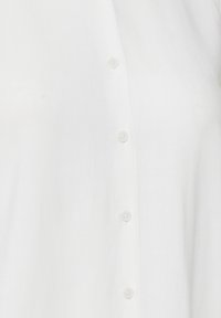 Vit skjorta med knäppning framtill i ett mjukt, lättviktigt tyg. Har små, runda knappar längs fronten för stängning. Enkelt design, inga mönster.