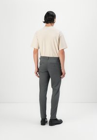Camiseta de manga corta en beige claro combinada con pantalones gris ajustados. Los pantalones tienen bolsillos y están diseñados con detalles minimalistas. Zapatos negros.