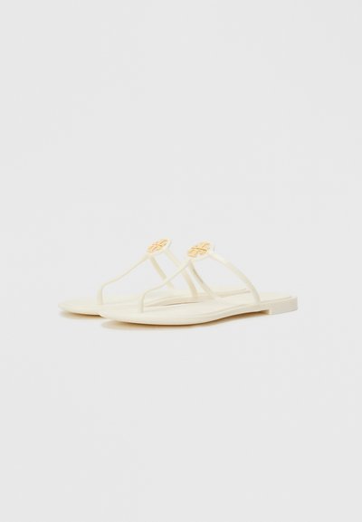 Flat sandals in creamy white with smooth texture, featuring narrow straps and a light orange accent detail. Simple, minimal design.