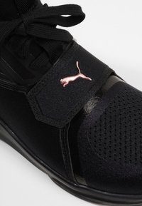 Musta urheilukenkä, jossa on teksturoitu verkko-osa, kiiltävät yksityiskohdat ja vaaleanpunainen Puma-logo hihnassa. Mukana nauhat ja pehmustettu kaulus.