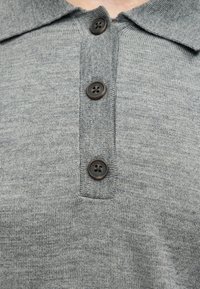 Κοντινό πλάνο γκρι πλεκτού τοπ με γιακά και τρία σκούρα κουμπιά στη μέση μπροστά.