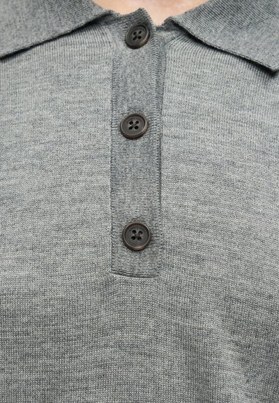 Κοντινό πλάνο γκρι πλεκτού τοπ με γιακά και τρία σκούρα κουμπιά στη μέση μπροστά.