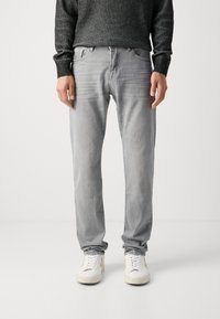 Jeans din denim gri cu o croială relaxată, talie medie și decolorare subtilă. Purtați cu adidași albi. O pulover texturat din tricot negru se află deasupra.