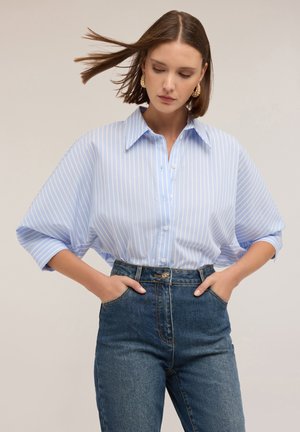 Camicia a righe blu e bianche con colletto a punta e maniche larghe, abbinata a jeans di jeans a vita alta.