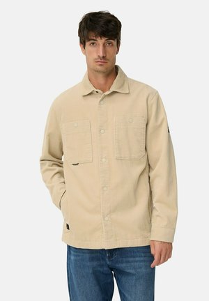 Beige corduroy jas met twee borstzakken, knoopsluiting en een zachte textuur. Draag over blauwe spijkerbroeken, met een casual pasvorm.