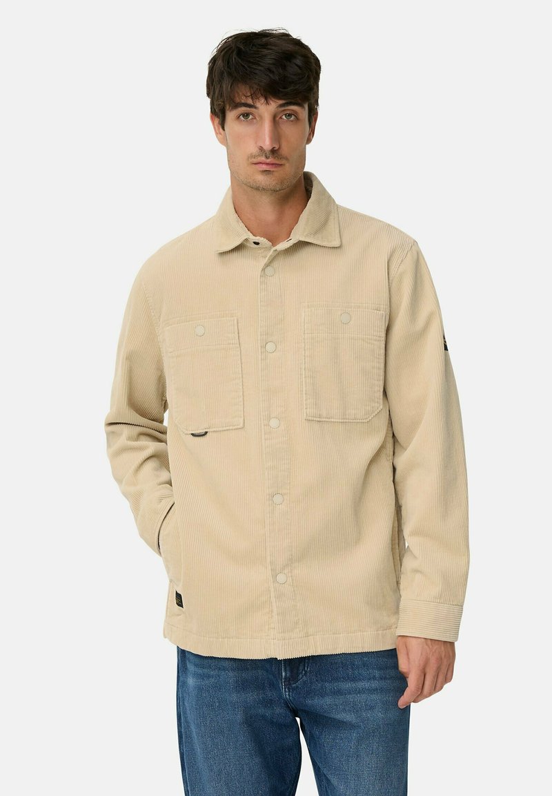 Beige corduroy jas met twee borstzakken, knoopsluiting en een zachte textuur. Draag over blauwe spijkerbroeken, met een casual pasvorm.