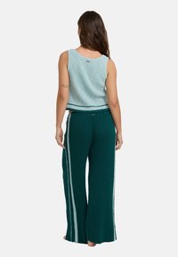 Lichtblauwe geribbelde gebreide crop top gecombineerd met donkergroene wijd uitlopende broek met een gestructureerd patroon en witte zijkanten.