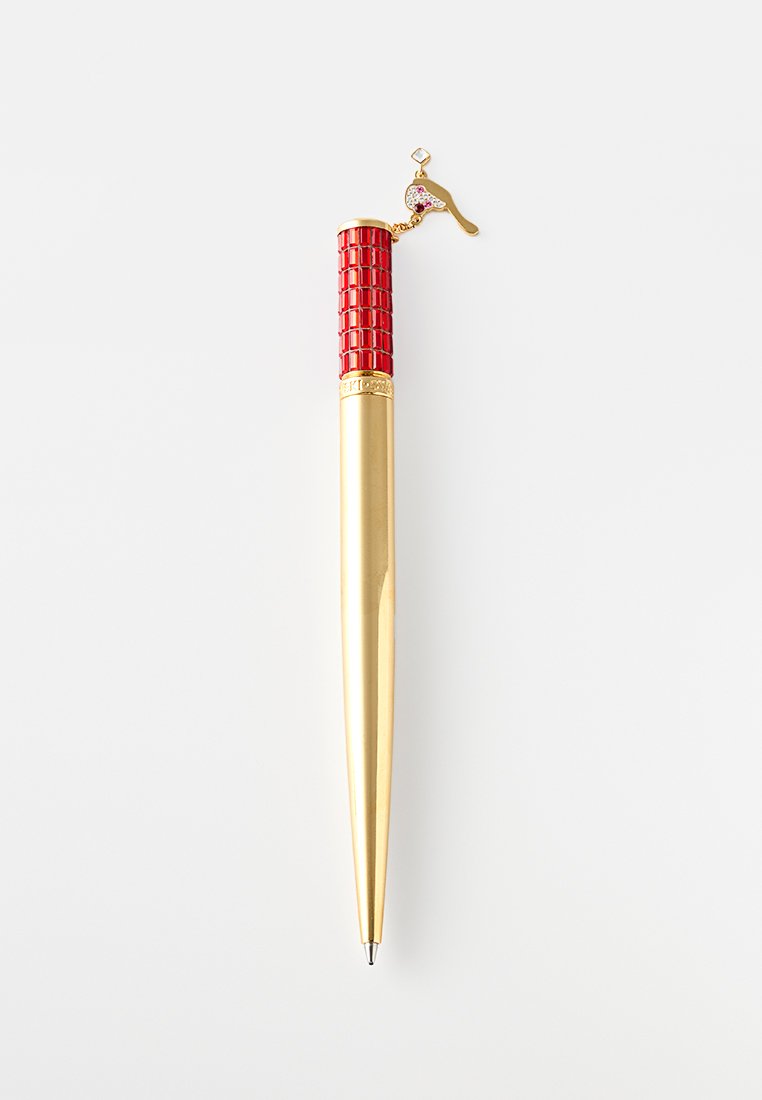 Bolígrafo dorado y rojo con empuñadura texturizada y un charm en forma de pájaro unido cerca de la parte superior sobre un fondo blanco.