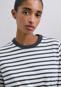 Camisa de manga larga a rayas en blanco y gris oscuro. Presenta un cuello redondo acanalado. Tejido suave con un corte holgado.