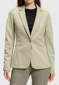 Blazer ajustado verde claro de tela suave, con solapas de muesca, cierre de botón único y dos bolsillos frontales.