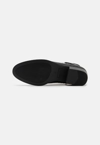 Suela de zapato negra con una superficie de goma texturizada que presenta ranuras horizontales y verticales, y una sección lisa cerca del talón.