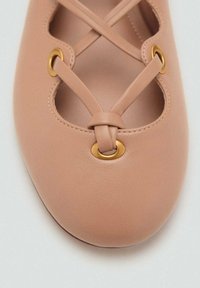 Bailarinas de cuero nude sin tacón con diseño de tiras cruzadas, corte ovalado y acentos en oro. Textura suave y forma de punta redonda.