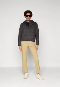 Čierna páperová bunda s kapucňou a predným zapínaním, hnedé priliehavé nohavice a krémové tenisky, s hladkou textúrou a priliehavým strihom.