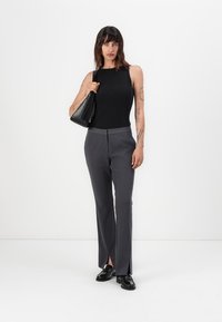 Sivé prispôsobené nohavice so bočnými rozparkom, v kombinácii s čiernym ribbed topom a čiernymi koženými topánkami. Modelka drží malú čiernu kabelku.