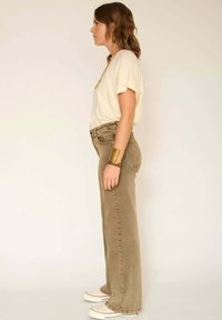 T-shirt beige clair, jean large kaki, et baskets blanches. La tenue présente un design simple et une coupe décontractée, avec des accents minimalistes.