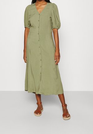 Olivgrünes Midi-Kleid, mit Knopfleiste vorne, V-Ausschnitt, Puffärmeln, leichtem Stoff und einem schwingenden Rockdesign. Kombiniert mit braunen Sandalen.