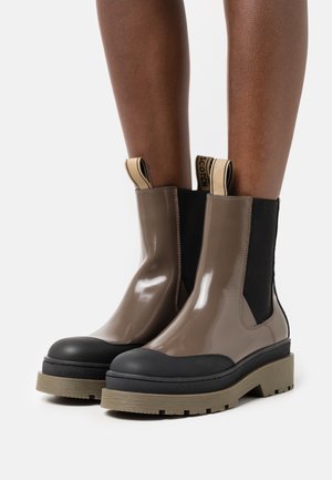 Bottes chelsea marron brillantes avec embout noir, semelle en caoutchouc texturée, panneaux latéraux élastiques et languettes de tirage contrastantes.
