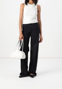 Top sin mangas de canalé blanco con escote redondo y adornos, combinado con pantalones de pierna ancha negros de cintura alta y un bolso estructurado blanco.