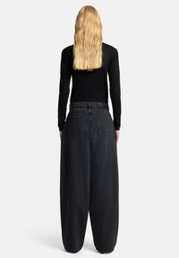 Czarne jeansy z szerokimi nogawkami i wysokim stanem, z tylnymi kieszeniami i luźnym krojem, zestawione z czarną bluzką z długim rękawem.